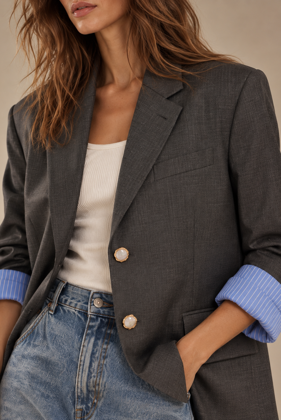 Close-up of charcoal blazer with gold pearlescent buttons and blue striped rolled cuffs