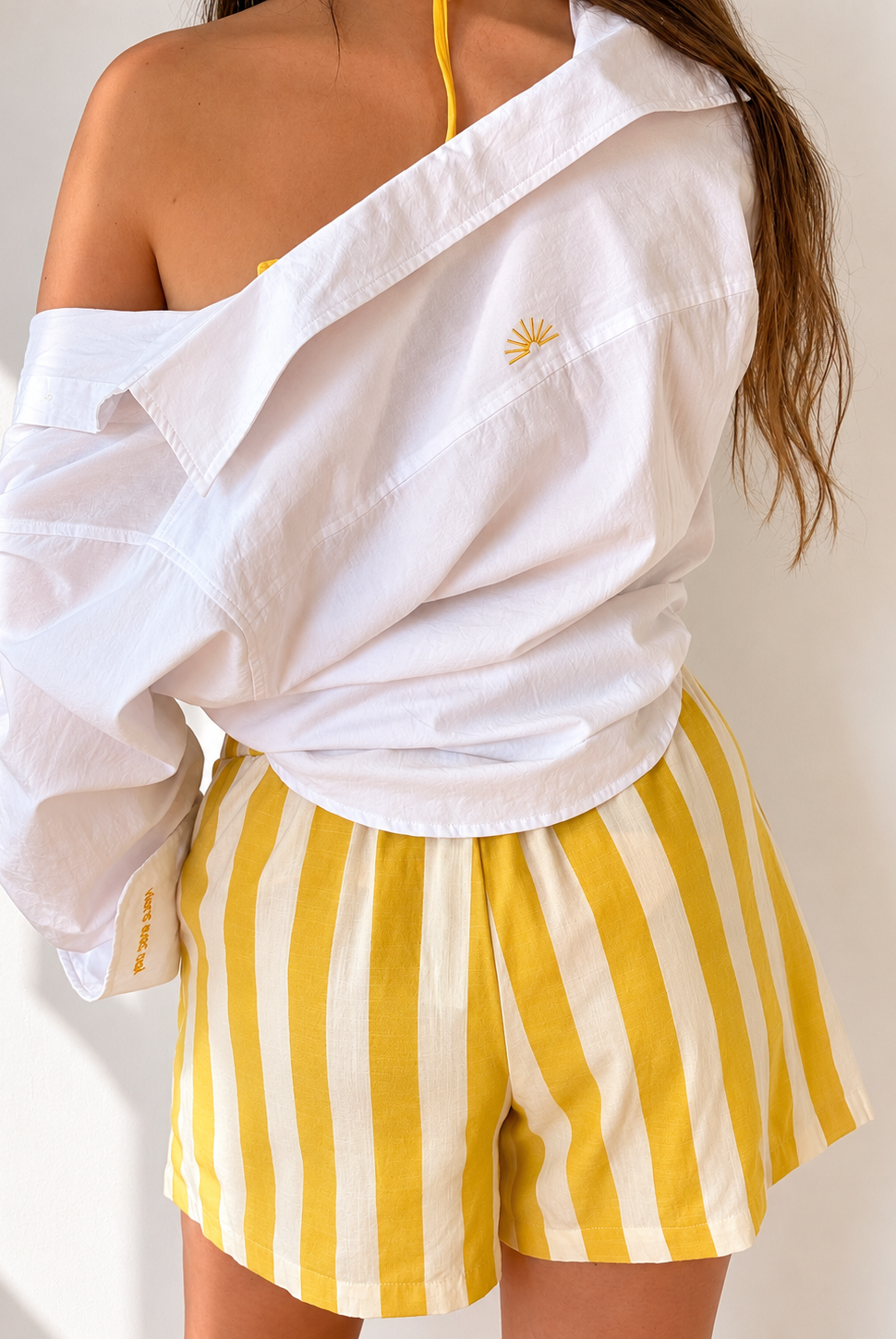 White embroidered cotton Everyday Boyfriend Shirt with sunset detail, paired with yellow striped shorts.
