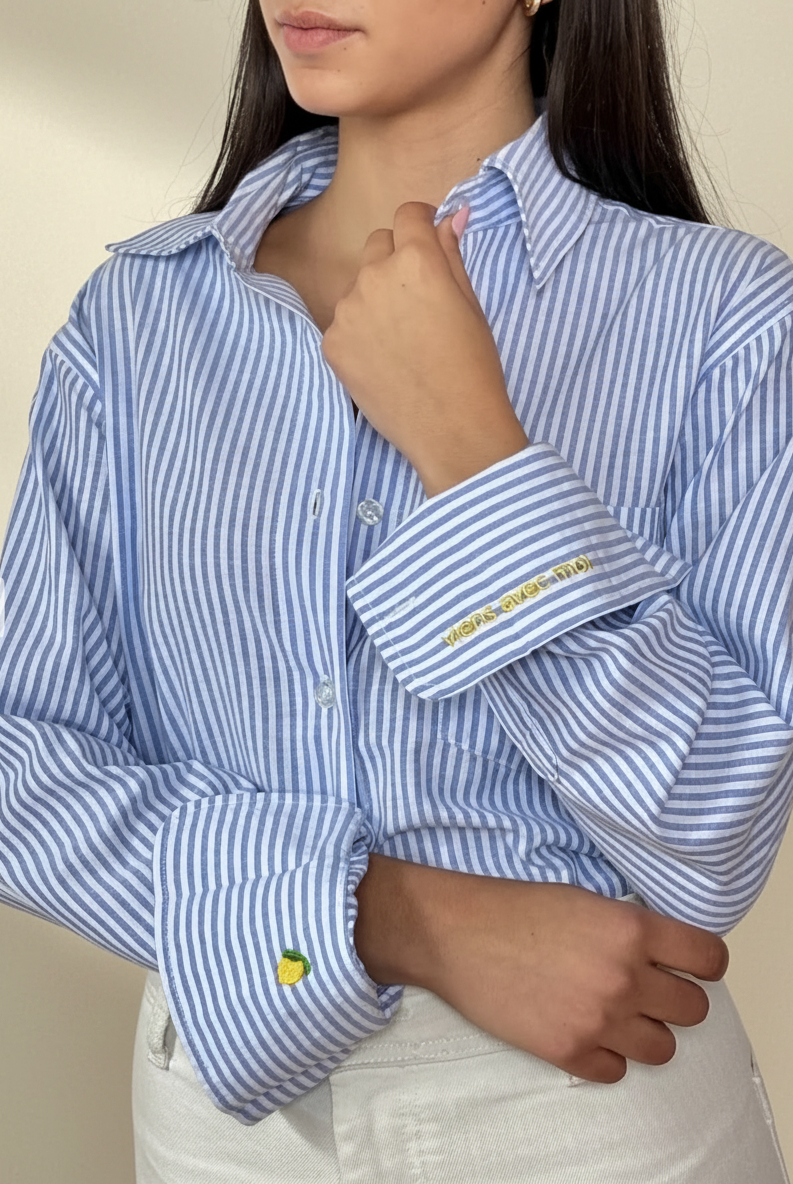 Woman wearing a blue and white striped shirt with embroidered details on a beige background