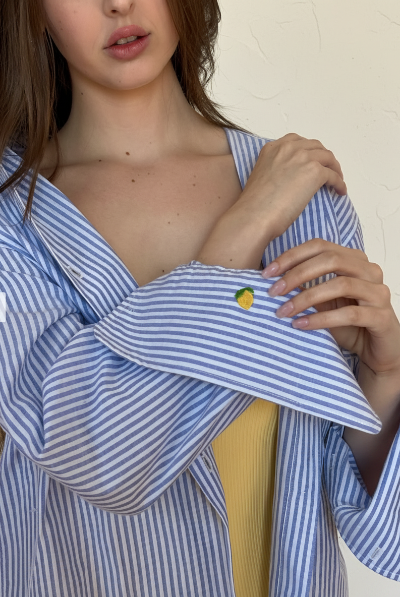 Person wearing a blue and white striped shirt holding a folded garment with a small embroidered lemon.