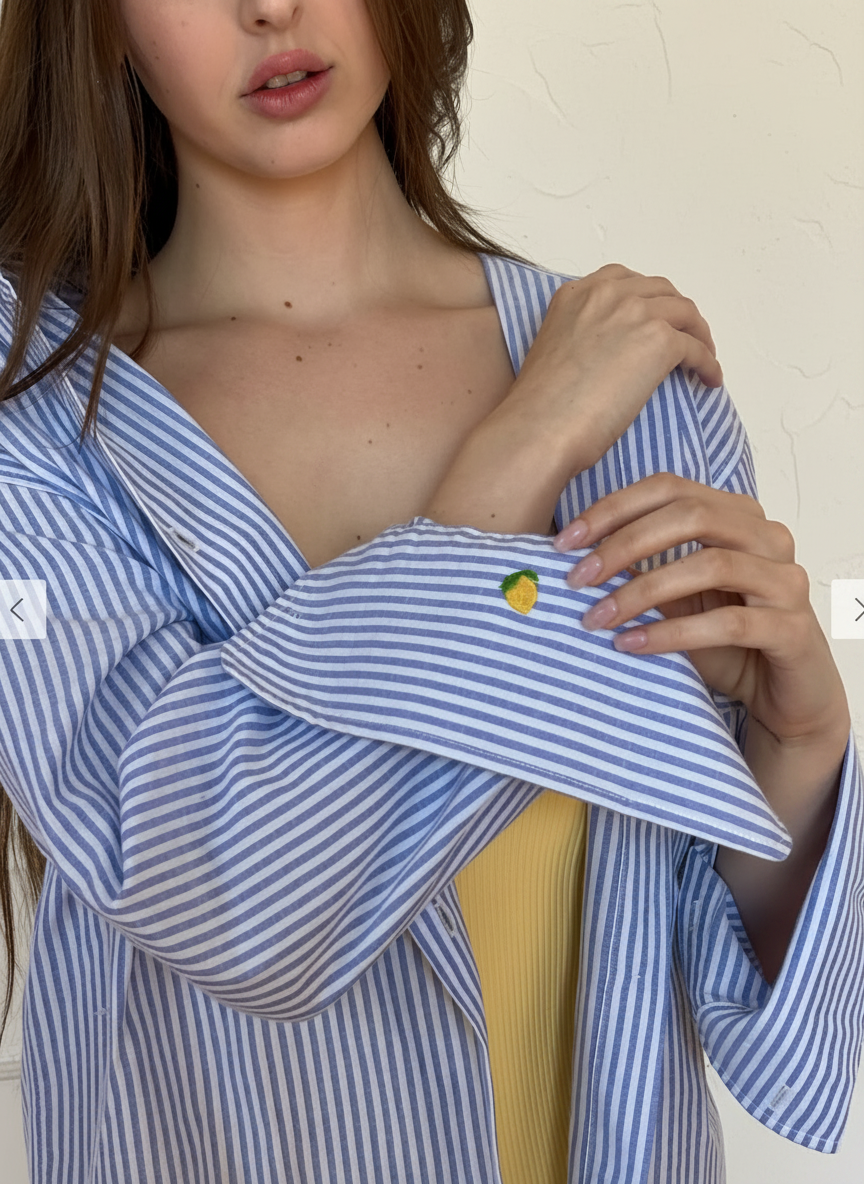 Person wearing a blue and white striped shirt holding a folded garment with a small embroidered lemon.