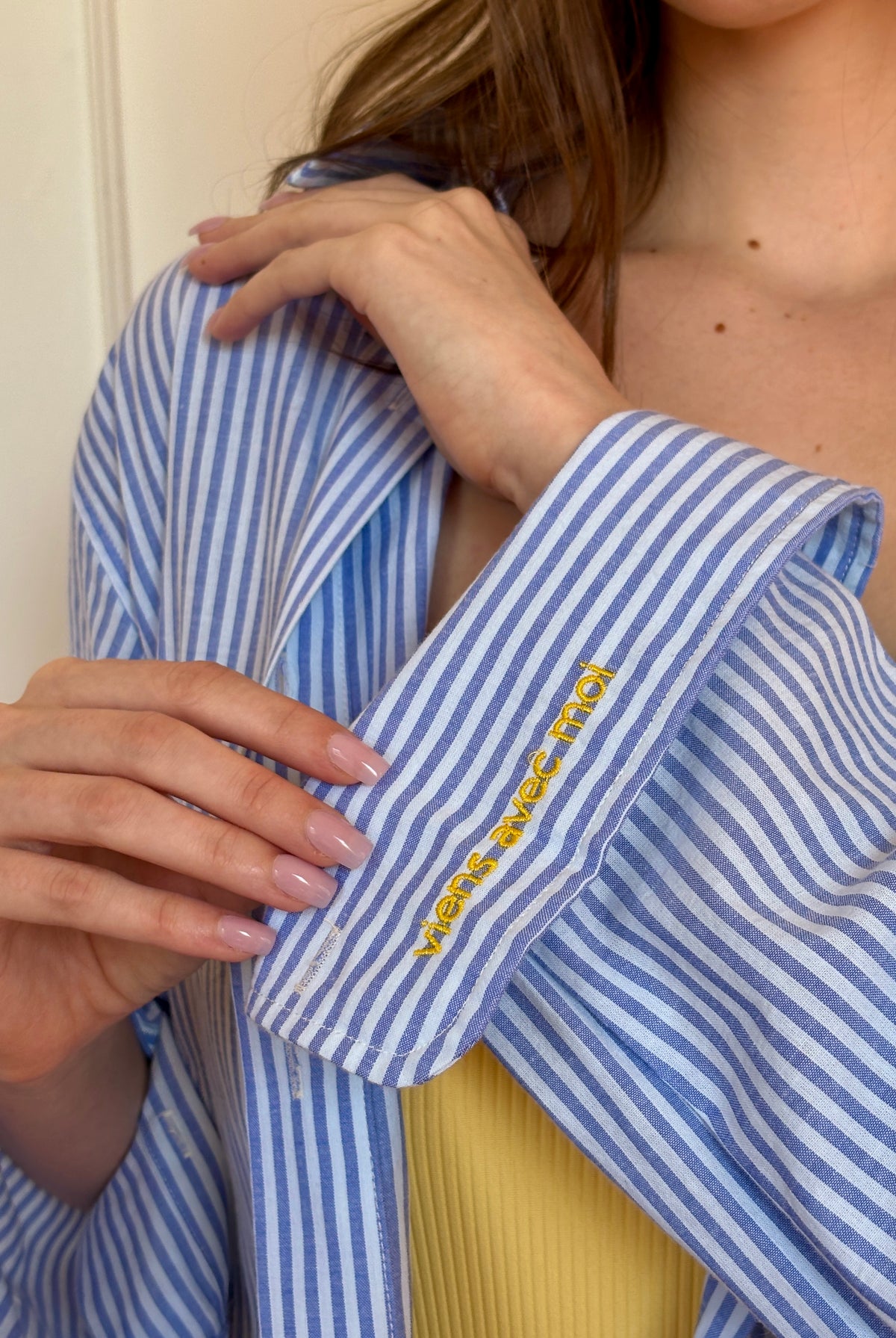 Person wearing a blue and white striped shirt with yellow embroidery, holding it open.