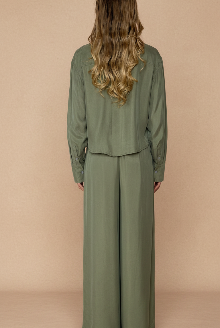 Woman wearing a green outfit with wide-leg pants against a beige background