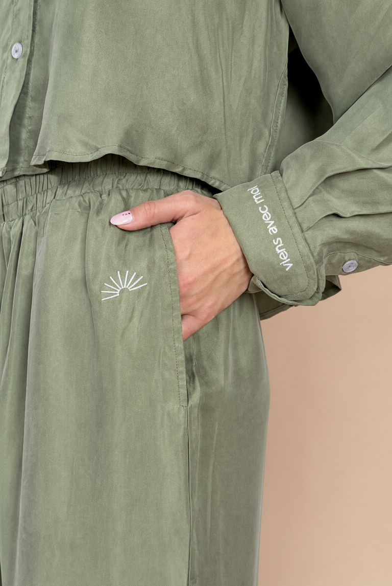 Green outfit with embroidered design and brand name on a neutral background