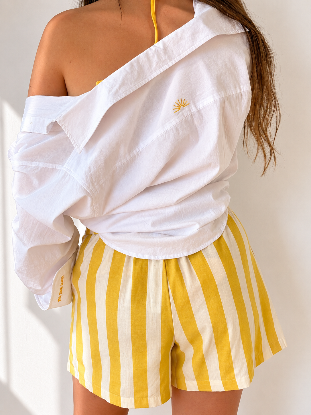 White embroidered cotton Everyday Boyfriend Shirt with sunset detail, paired with yellow striped shorts.