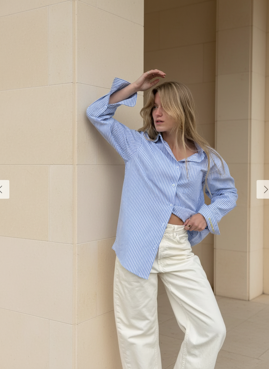 Woman wearing a blue checkered shirt and white pants against a beige wall.
