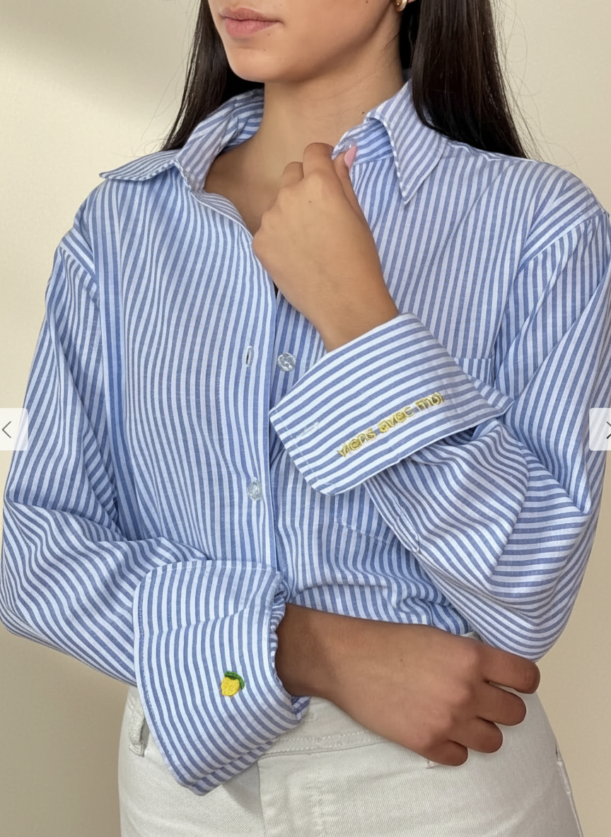 Woman wearing a blue and white striped shirt with embroidered details on a beige background