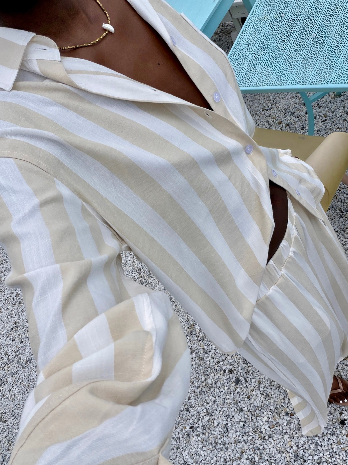 Close-up of a person wearing a white and beige striped shirt on a textured surface.