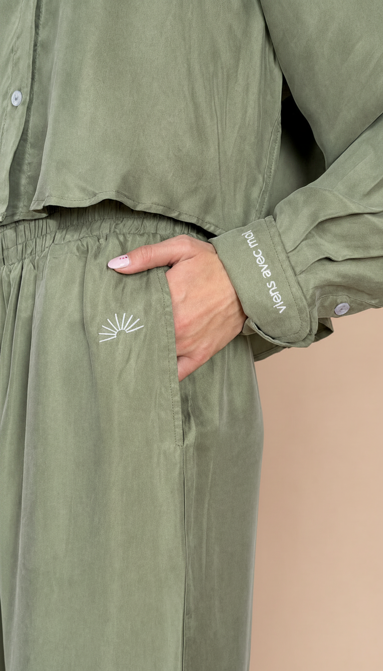 Green outfit with embroidered design and brand name on a neutral background