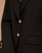 Close-up of black pinstripe blazer with gold and black enamel crest buttons and flap pocket